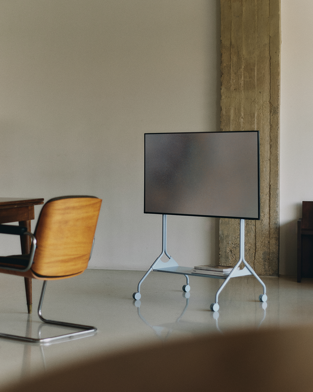 Moon Tray Shelf in Powder Blue holding magazines on a rolling TV stand in a minimal concrete-and-plaster living space