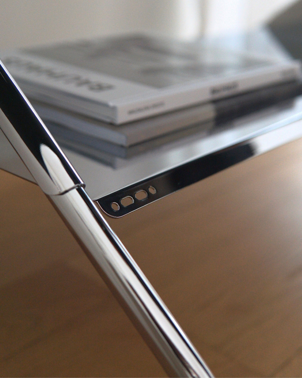 Close-up of Moon Tray Shelf in Chrome, showing polished edge detail and slotted bracket with stacked books above