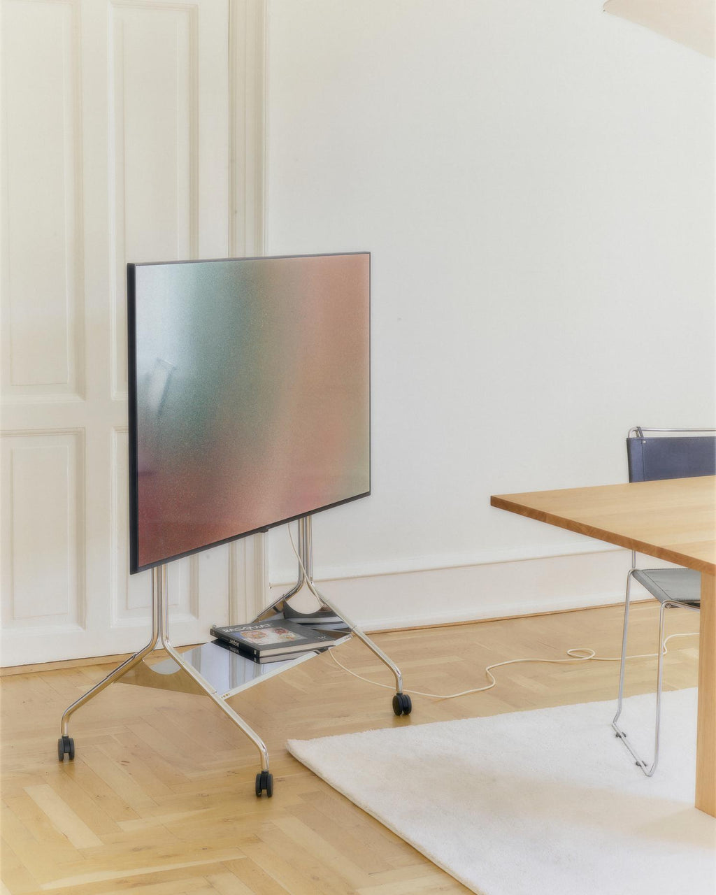 Moon Tray Shelf in Chrome holding art books beneath a TV on a rolling floor stand in a bright paneled dining room