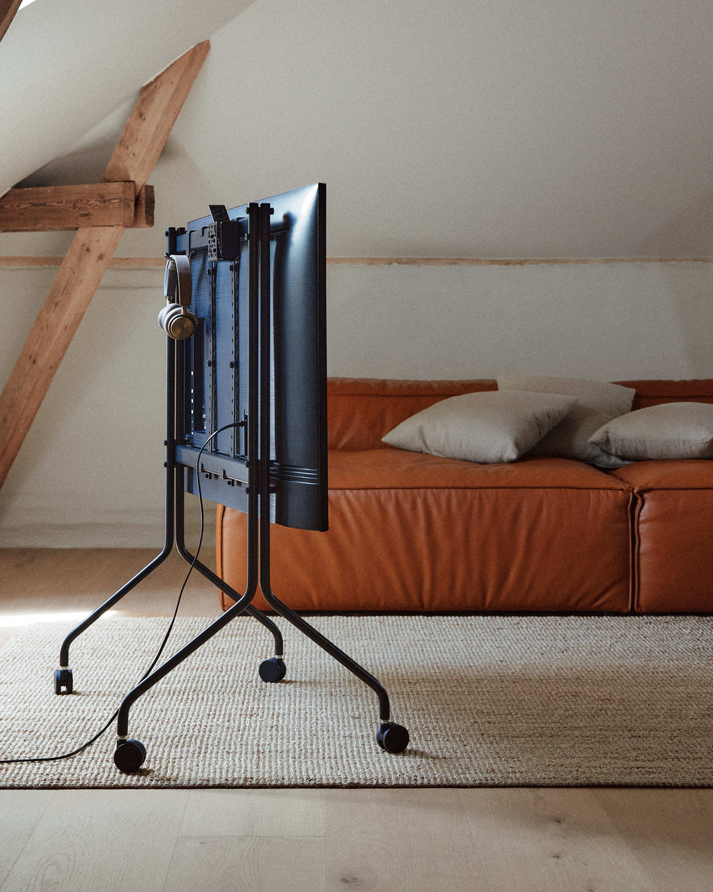 Charcoal Mount Bundle rear view on wheels in attic lounge, TV back and headphones visible beside a tan leather sofa