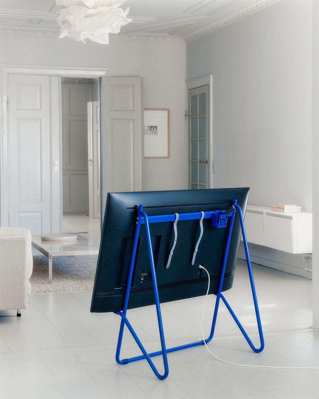 Ultra Marine Mount Bundle holding a large TV from behind in a bright white living room, easel-style legs in view