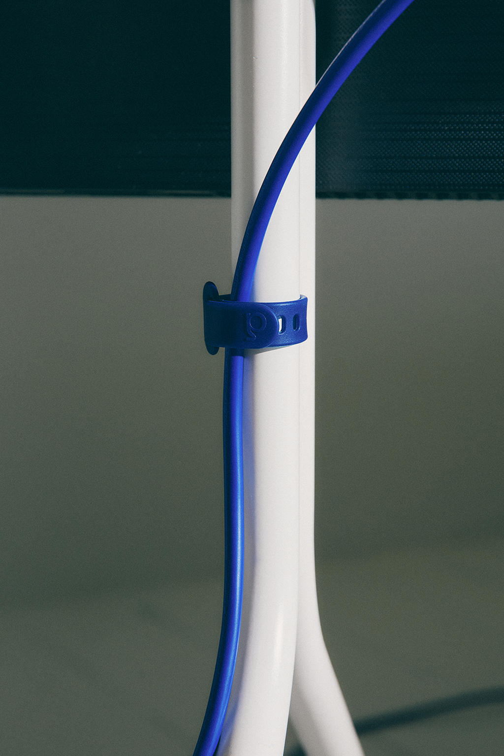 Close-up of the Ultra Marine Mount Bundle strap securing a blue cable to a white stand leg