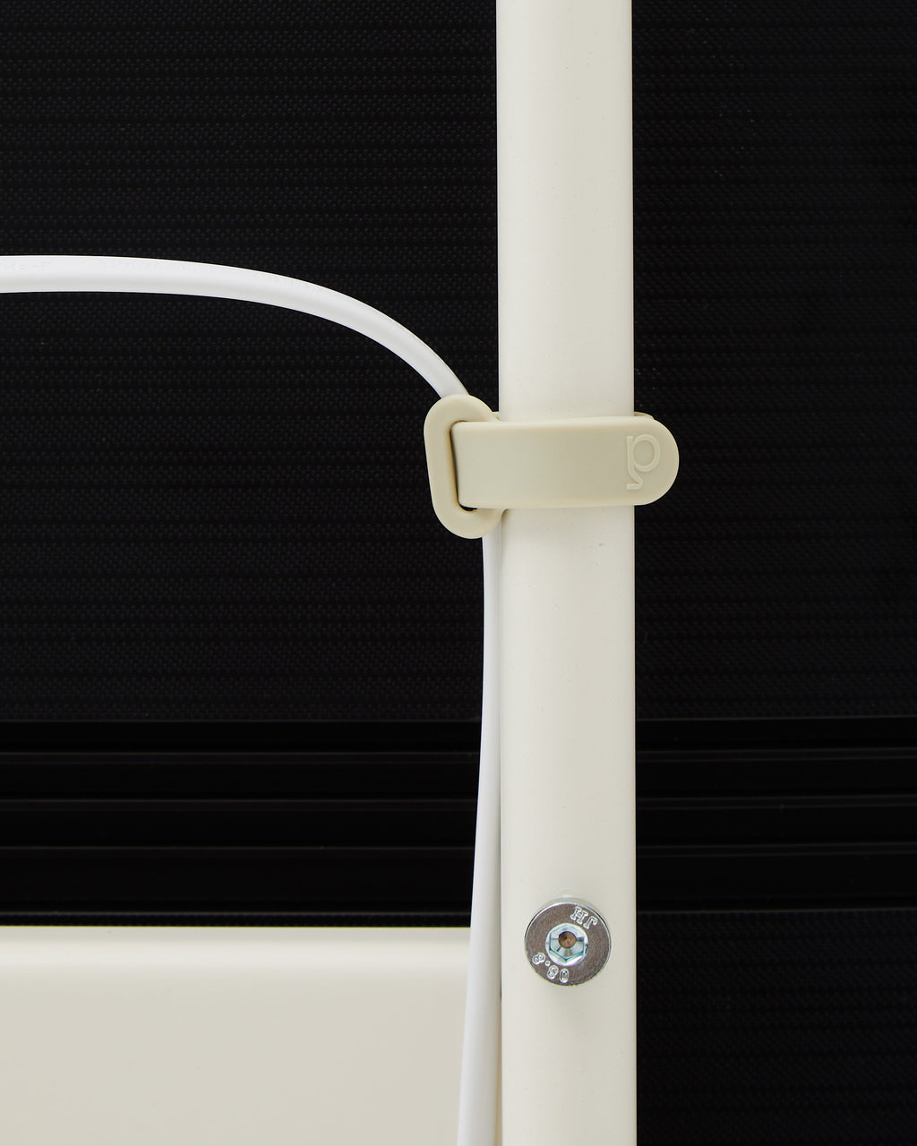 Close-up of Mount Bundle in Pearl cable clip securing a white cord to the vertical pole against a dark backdrop