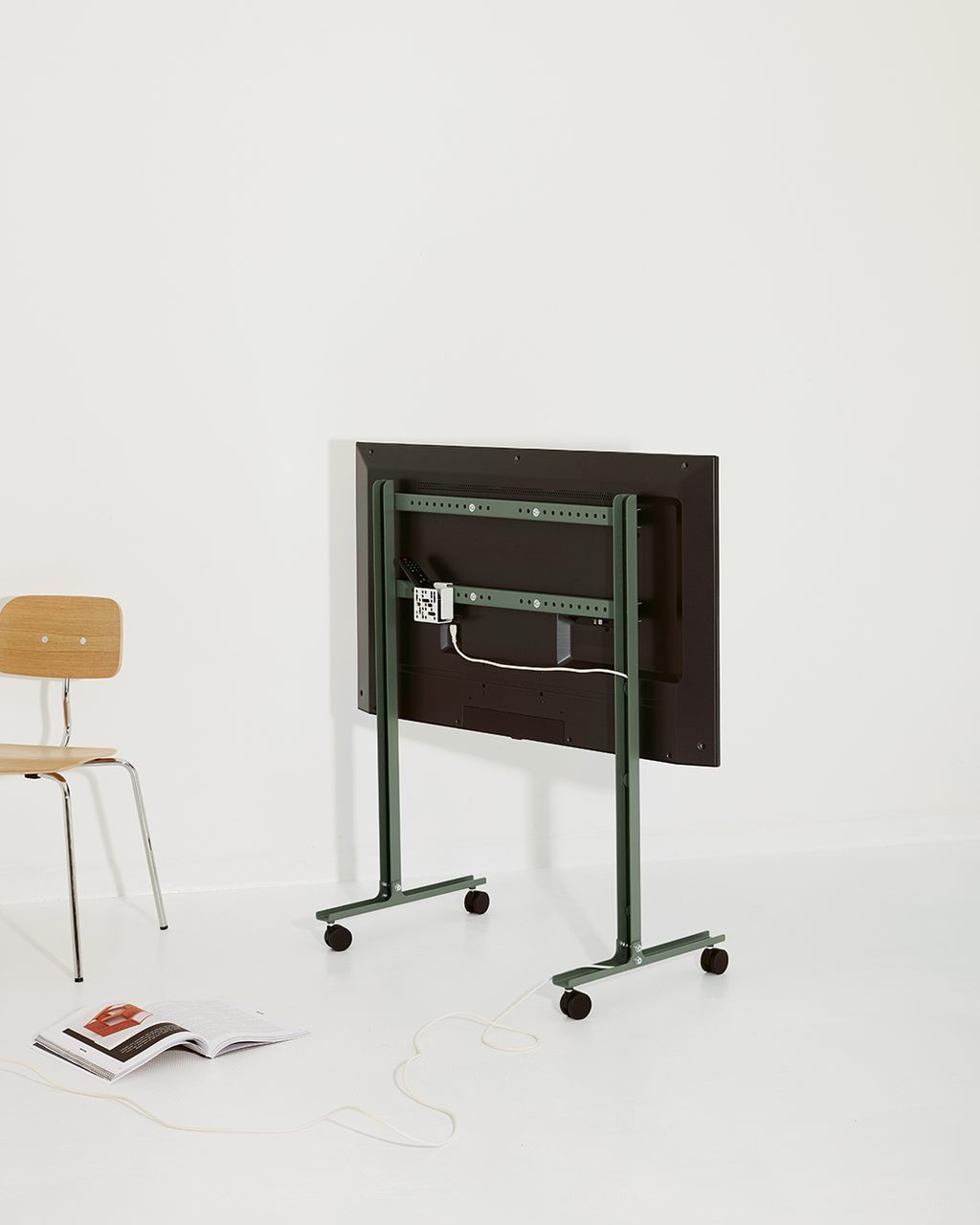 Rear view of a TV on the Mount Bundle in Pearl green rolling floor stand with casters, shown in a bright studio room