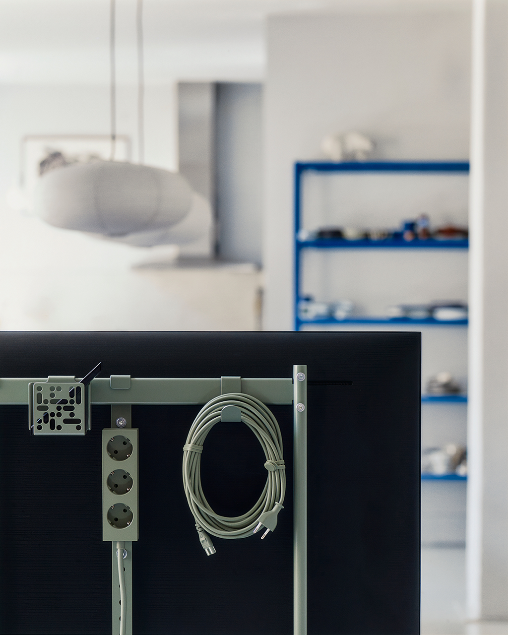 Mount Bundle in Mossy Green holding a coiled cable and power strip on a TV's rear frame in a bright studio room