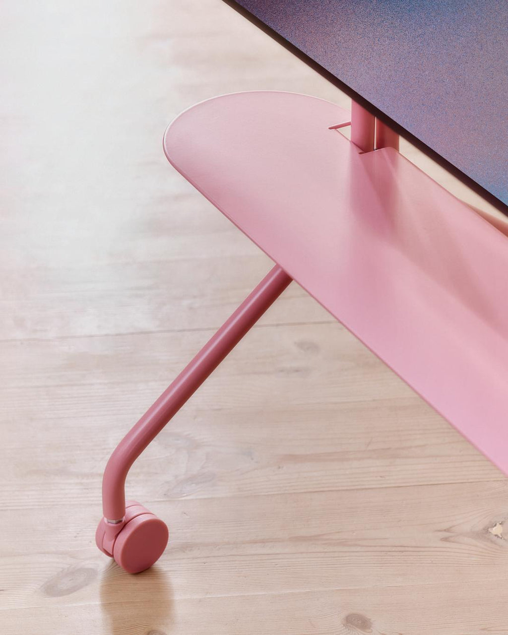 Close-up of Moon Shelf in Bubble Gum, showing curved pink base leg and caster wheel on light wood floor under a display
