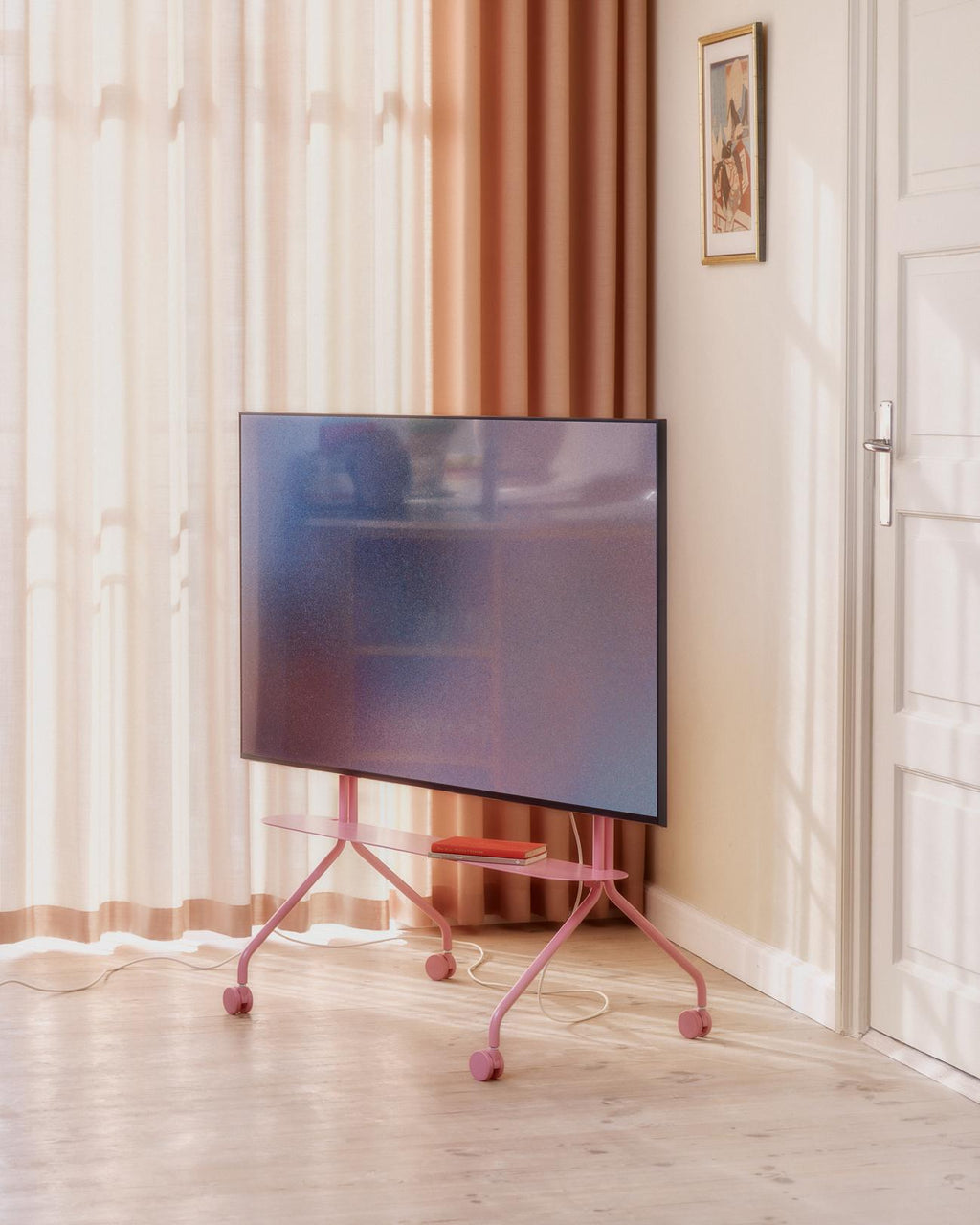 Bubble Gum Moon Shelf on a rolling pink TV stand in a sunlit room, holding a red book beneath a mounted screen