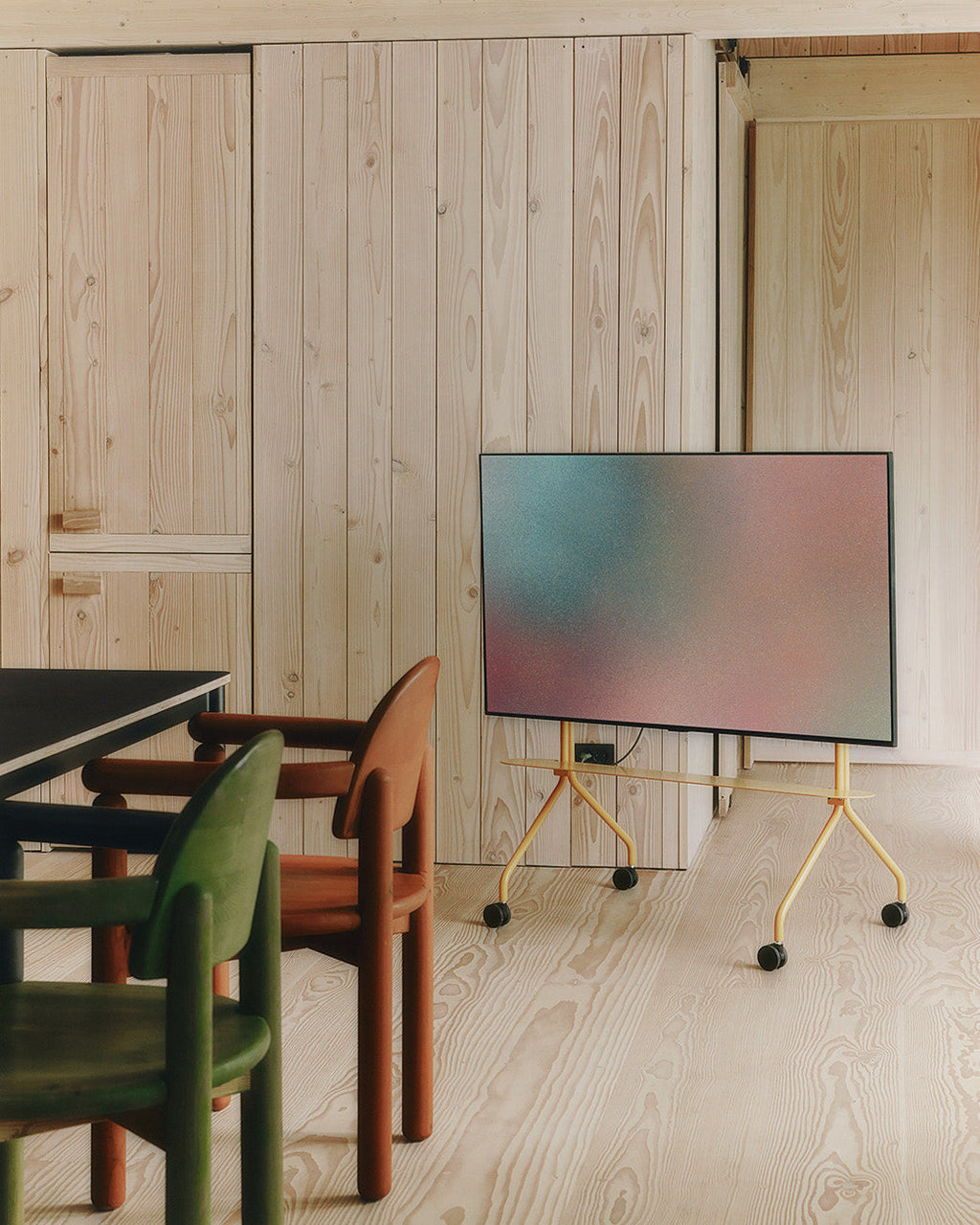 Moon Shelf in Apricot on wheels holding a mounted TV in a pine-clad room with green and terracotta chairs