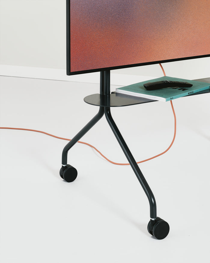Moon Shelf in Oat holding magazines and a remote on a black rolling TV stand, low-angle studio view with casters