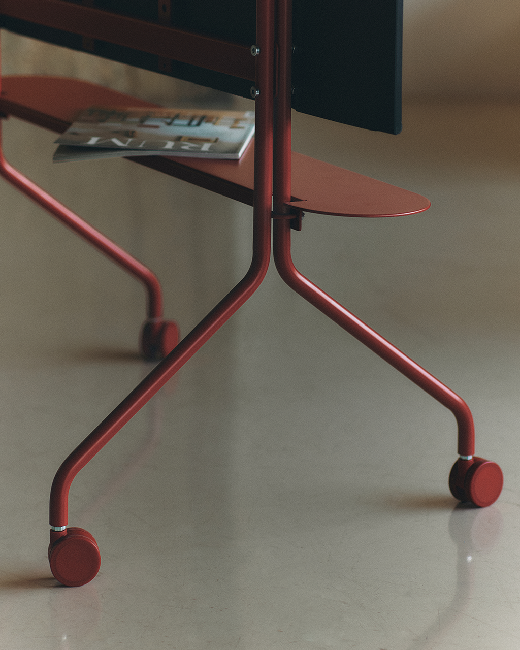 Close-up of the Moon Shelf in Burnin' Red, showing its red tubular legs, castor wheels and magazine on the lower tray