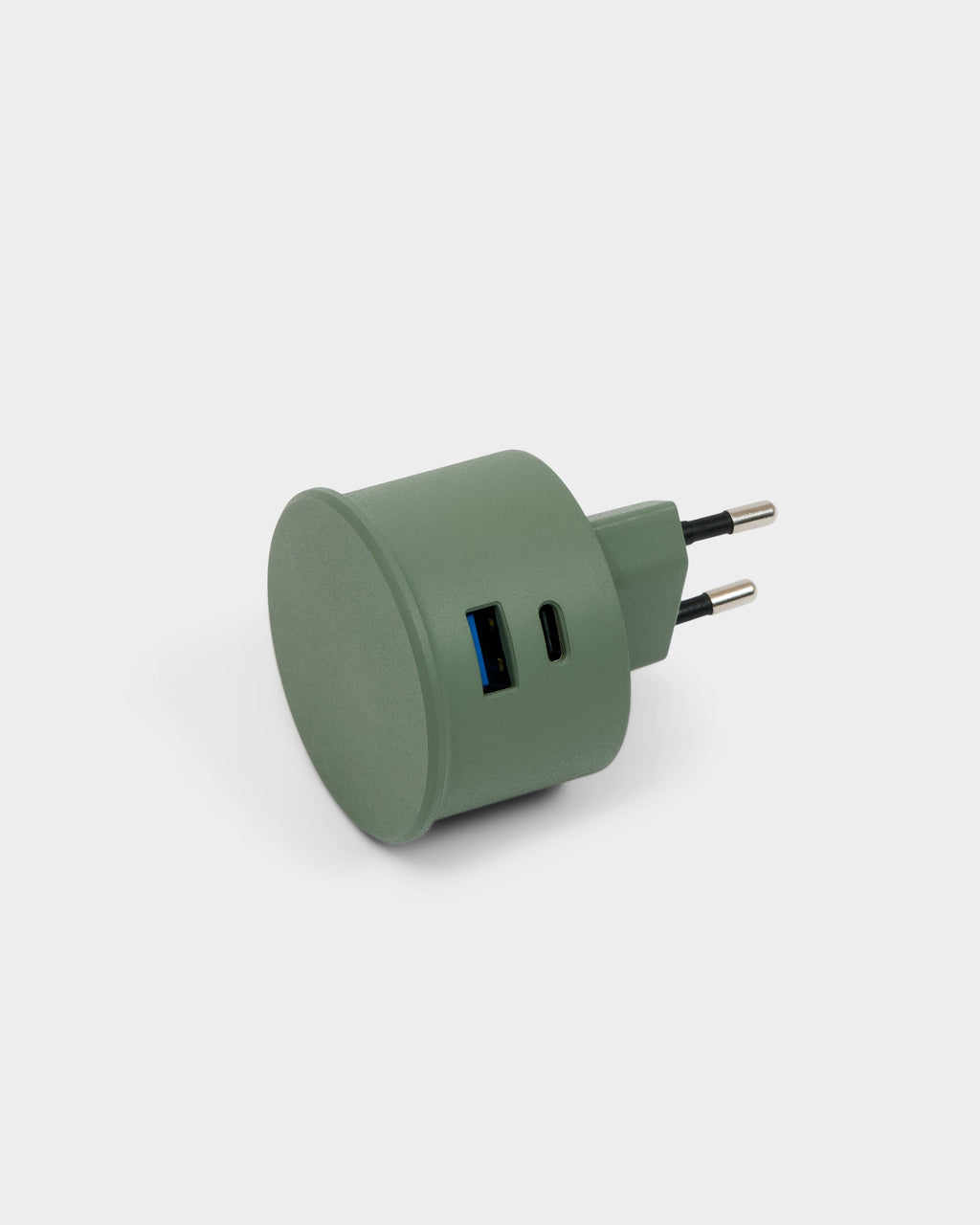 Mossy Green power adapter in a studio packshot, angled to show USB-A and USB-C ports plus dual European prongs