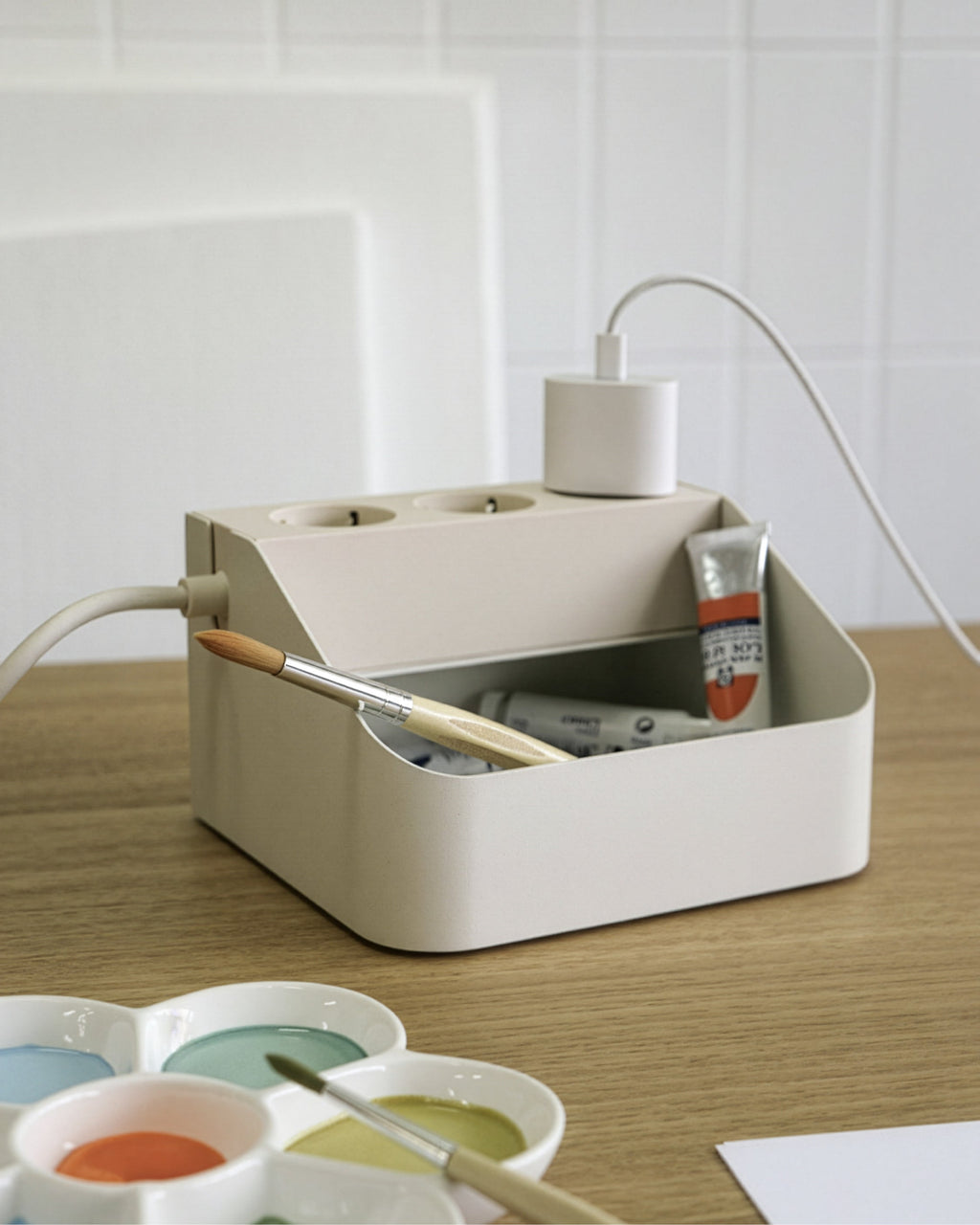Pearl Power Bar Tray on an oak desk holding paint tubes and a brush, with a charger plugged into its sockets