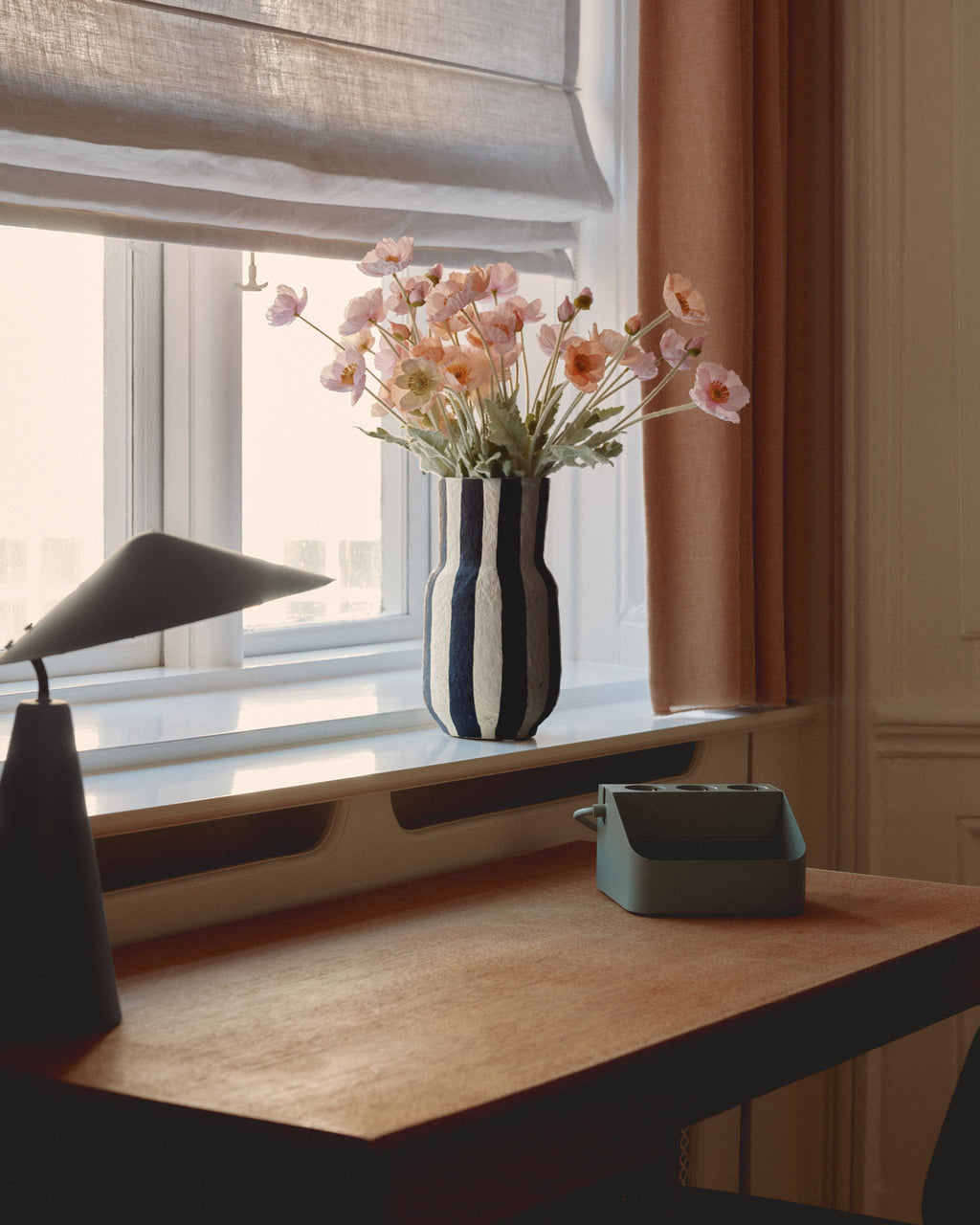 Mossy Green Power Bar Tray on a sunlit wooden desk beside a window, striped vase of pink poppies behind it