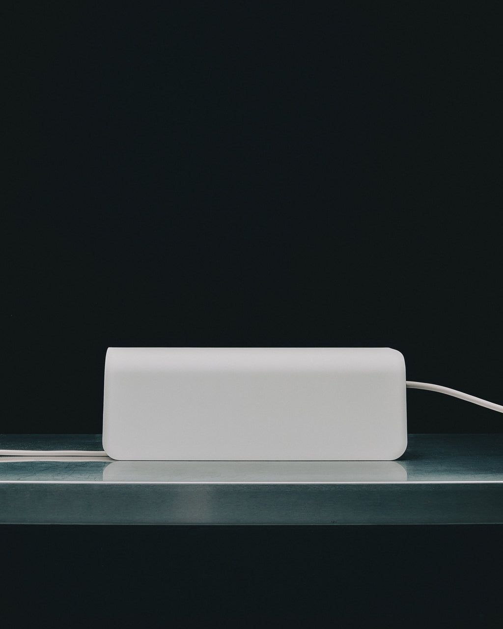 Power Shell in Pearl viewed side-on atop a steel shelf against a dark backdrop, white cable trailing out to the right