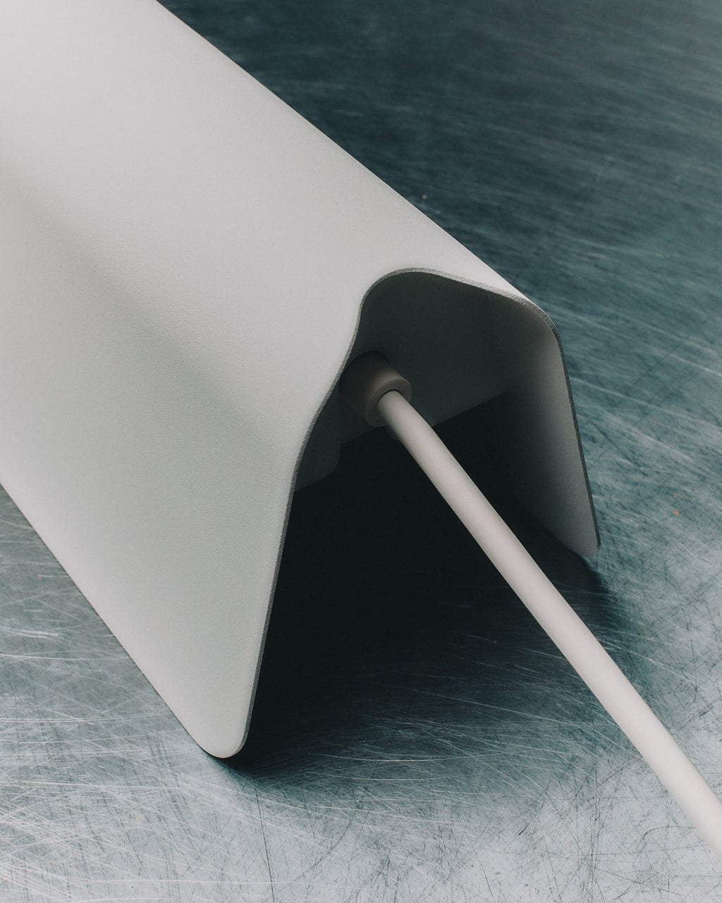 Close-up of Power Shell in Pearl on scratched metal, showing cable exit port beneath the angled shell edge