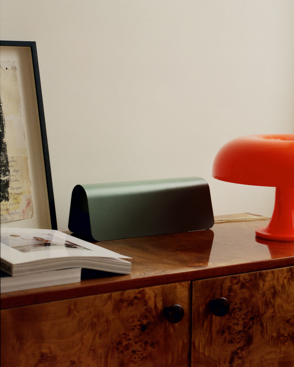 Mossy Green Power Shell on a burl wood sideboard beside a red mushroom lamp, framed art and open book