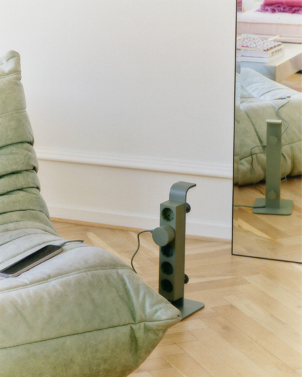 Mossy Green Power Tower standing on herringbone floor beside a sage sofa, reflected in a leaning floor mirror