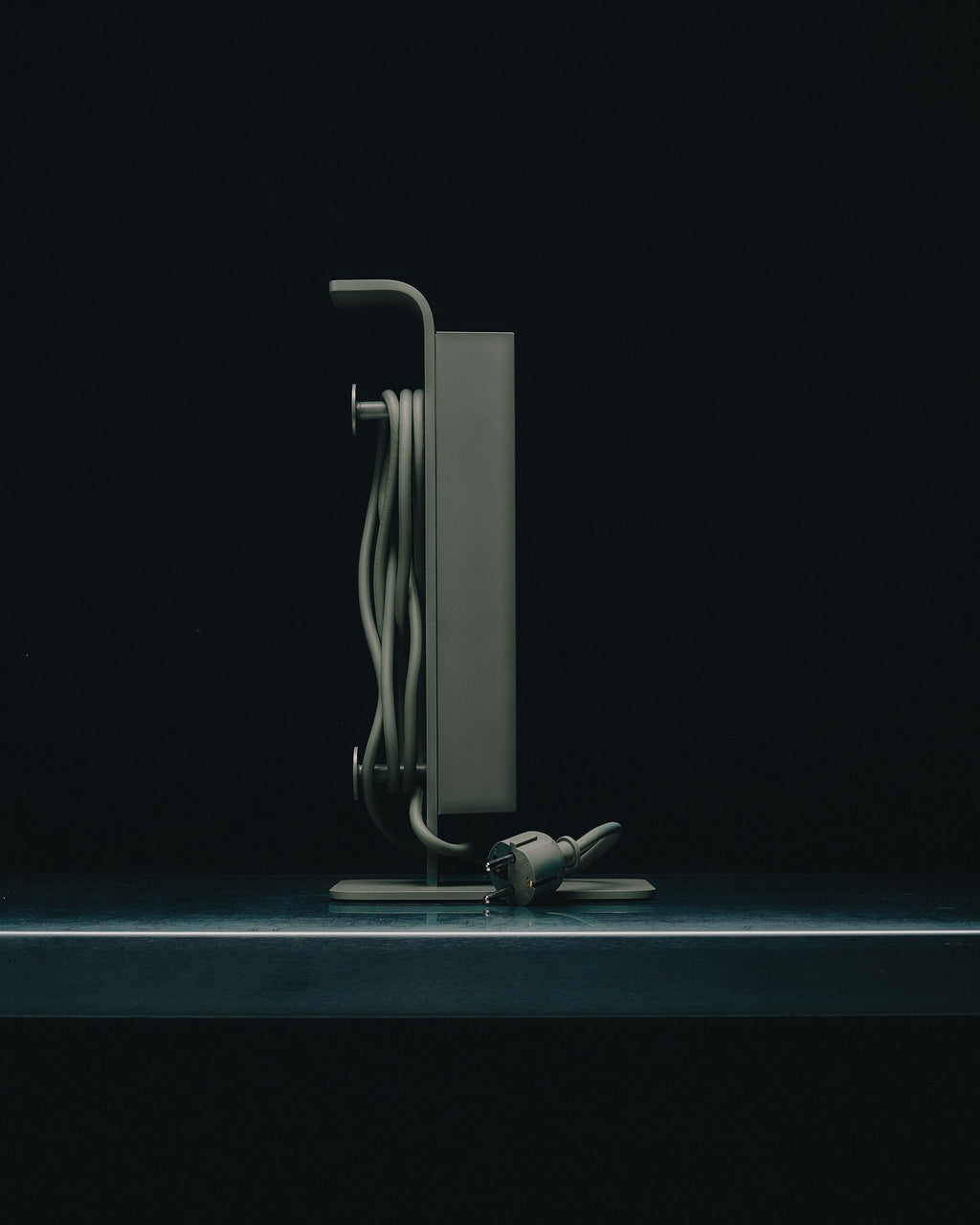 Side profile of the Power Tower in Mossy Green on a dark studio surface, cord neatly wound and plug resting at base
