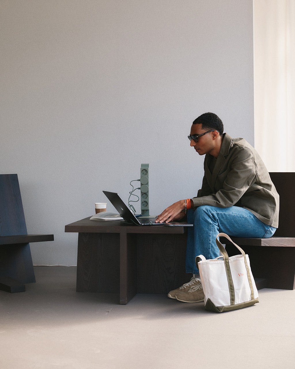 Man on laptop at dark wood table with Power Tower in Mossy Green plugged in beside him in a bright studio space