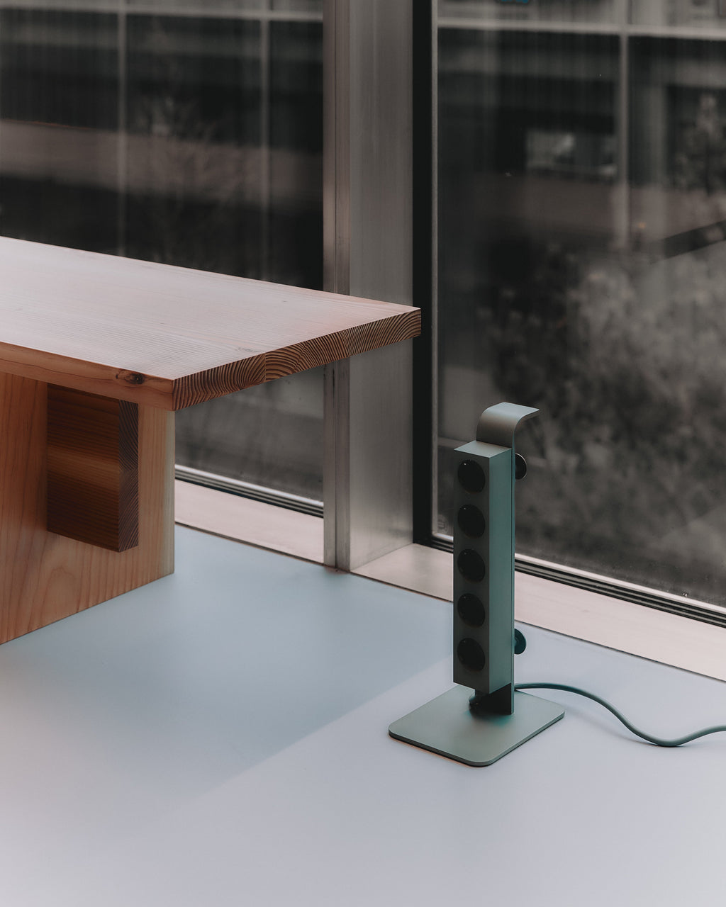 Mossy Green Power Tower standing on a pale windowsill beside a wooden desk, cord trailing across the surface