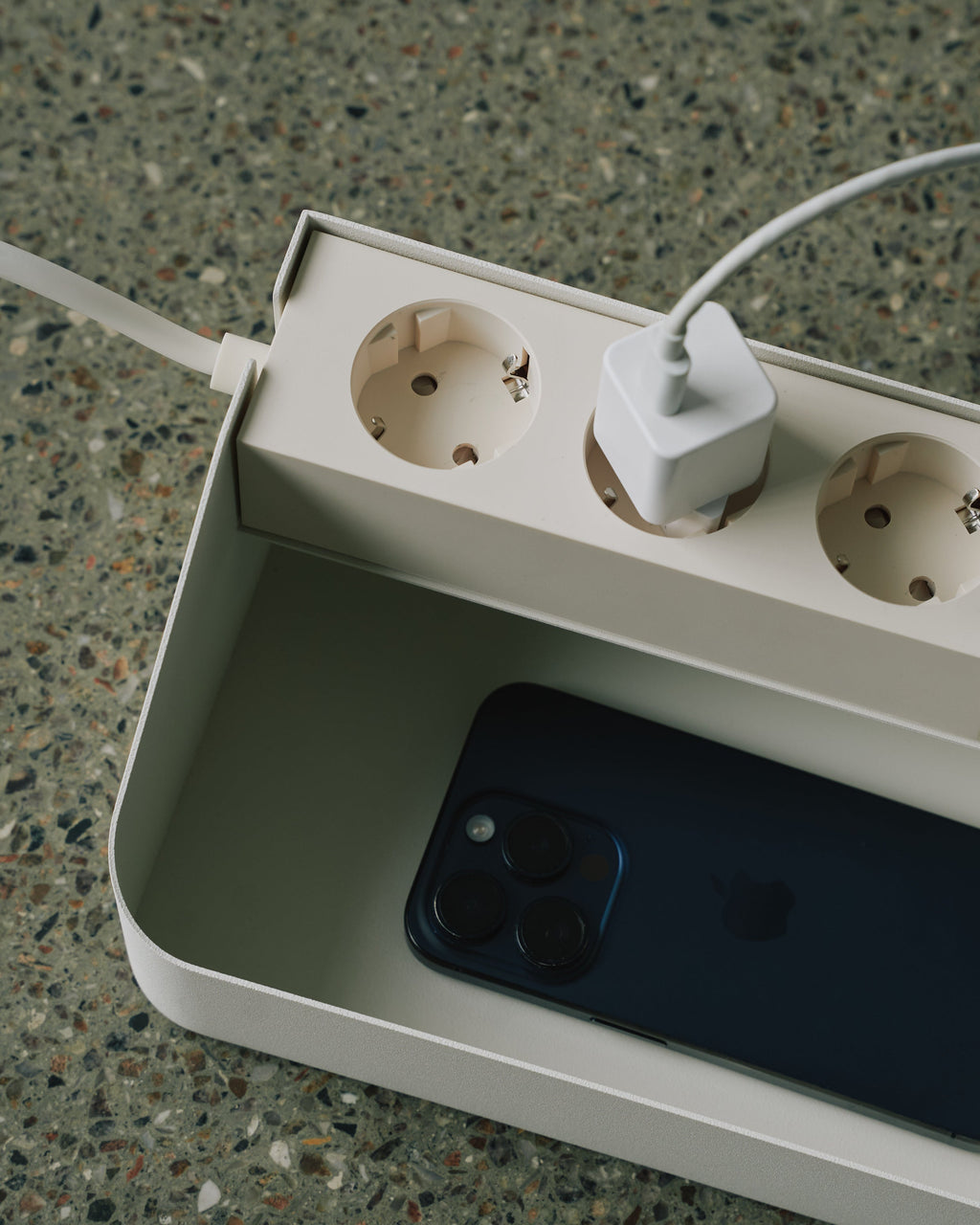 Power Beam Tray in Pearl on terrazzo, close-up angle showing three sockets, plugged charger and phone in the tray