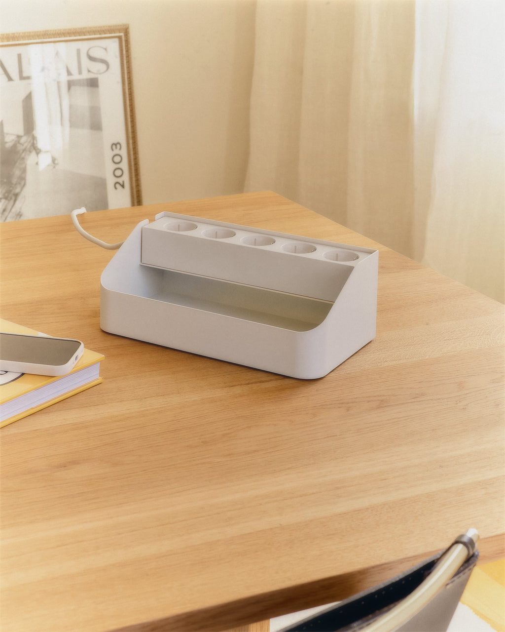 Power Beam Tray in Pearl on an oak desk, angled view showing five outlets and open storage trough beside a book