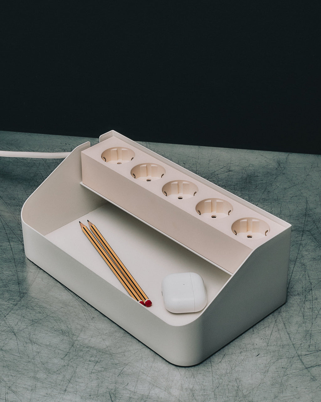Power Beam Tray in Pearl angled on a scratched grey surface, five sockets above a storage well holding pencils and earbuds
