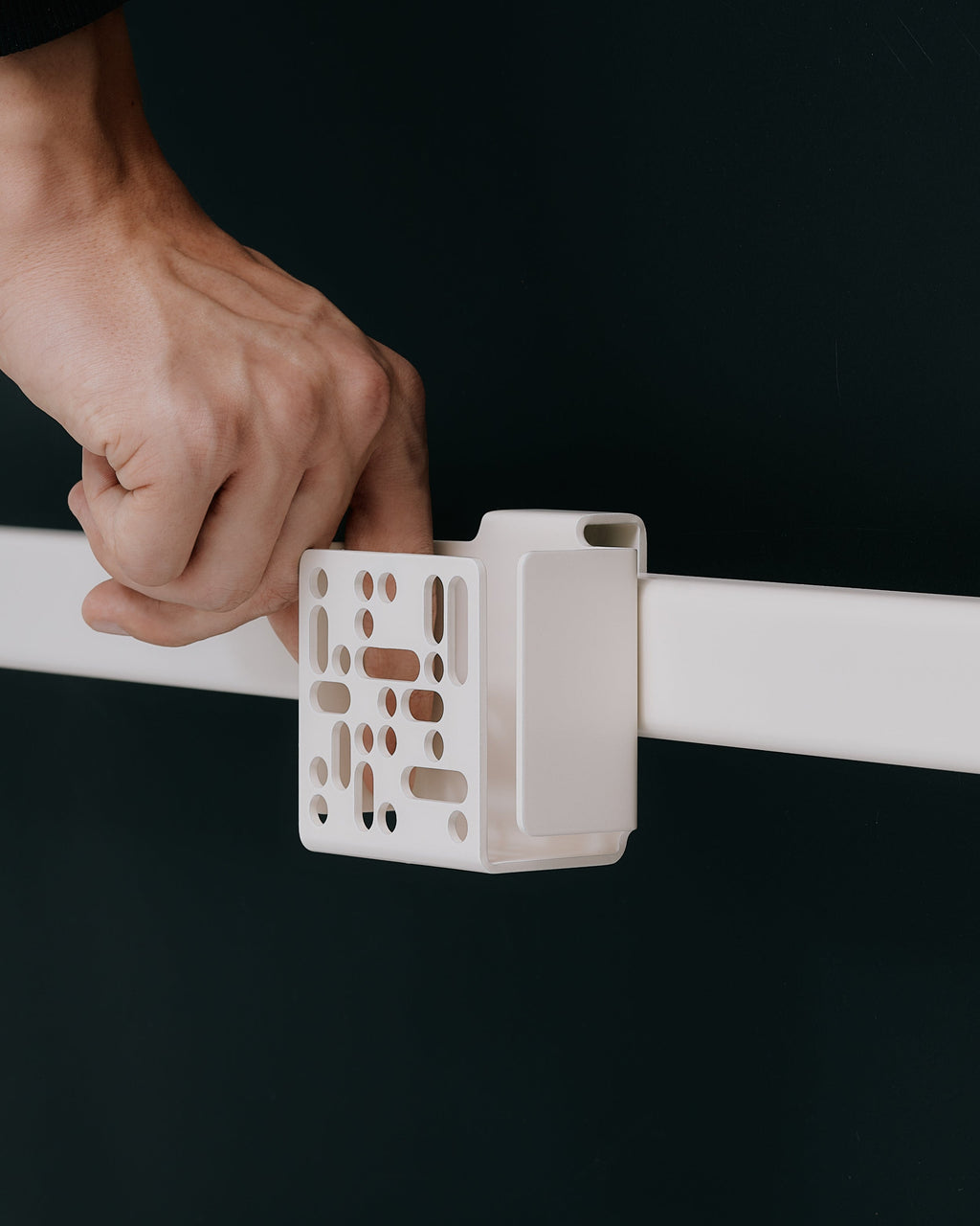 Hand sliding the Remote Box Mount in Charcoal onto a white rail against a dark studio backdrop, close side angle
