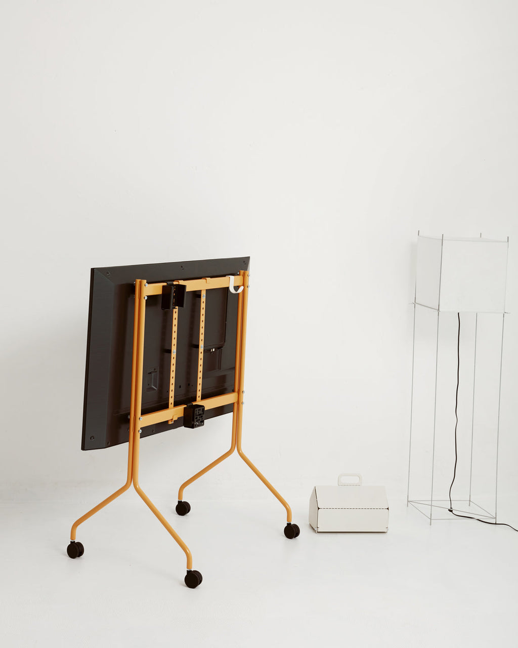 Rear view of Remote Box Mount in Charcoal on a yellow rolling TV stand in a bright studio with lamp and carry case