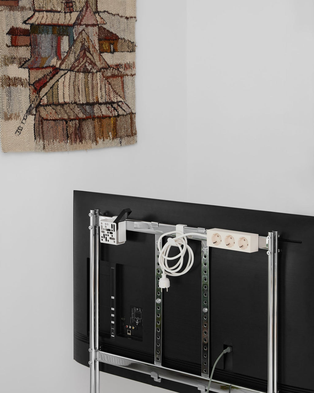 Pearl Remote Box Mount fixed to a TV stand rail behind a wall-mounted flat screen, with coiled cable and power strip