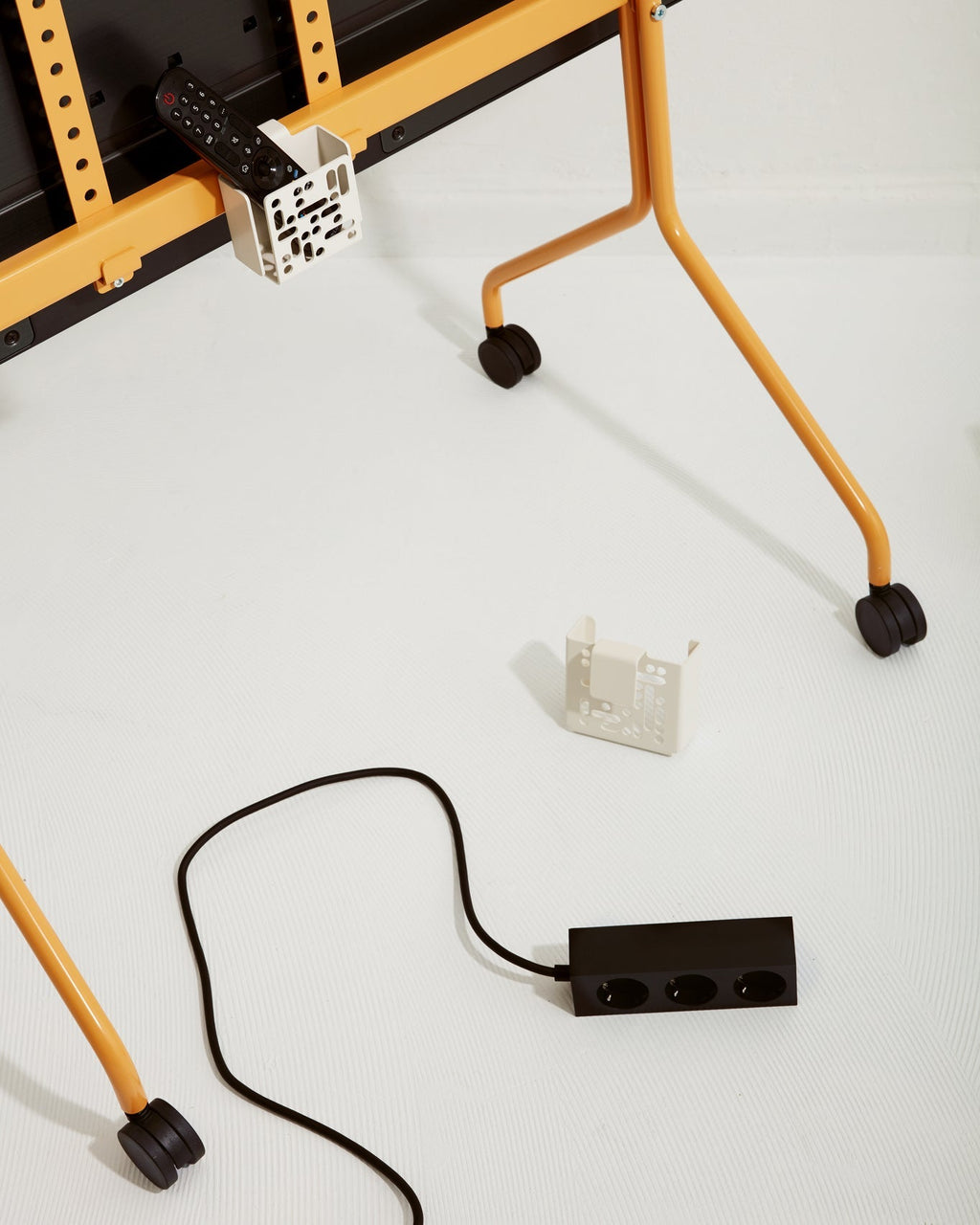 Pearl Remote Box Mount holding a remote on an orange TV stand, with a second mount and power strip on the floor
