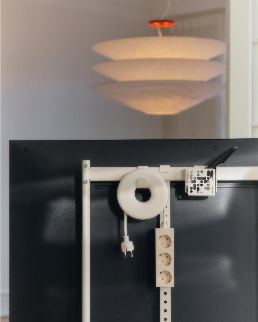 Pearl Remote Box Mount holding a remote on a rail behind a wall-mounted TV, with a pendant lamp glowing above