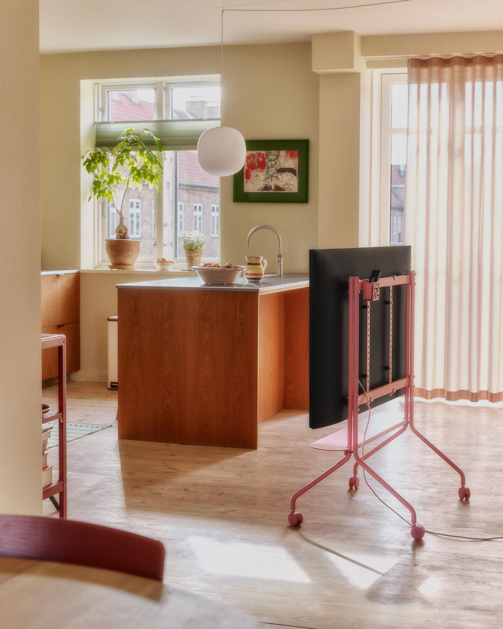 Bubble Gum Remote Box Mount holding a TV on a rolling pink floor stand in a sunlit kitchen living space