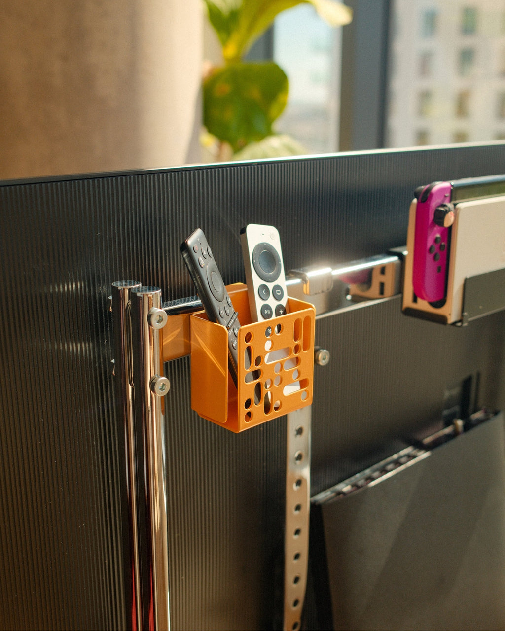 Apricot Remote Box Mount attached to a TV's rear edge, holding two remotes in a sunlit living room scene