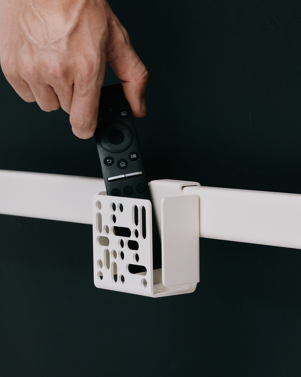 Hand sliding a remote into the Remote Box Mount in Mossy Green, clipped onto a white rail against a dark backdrop