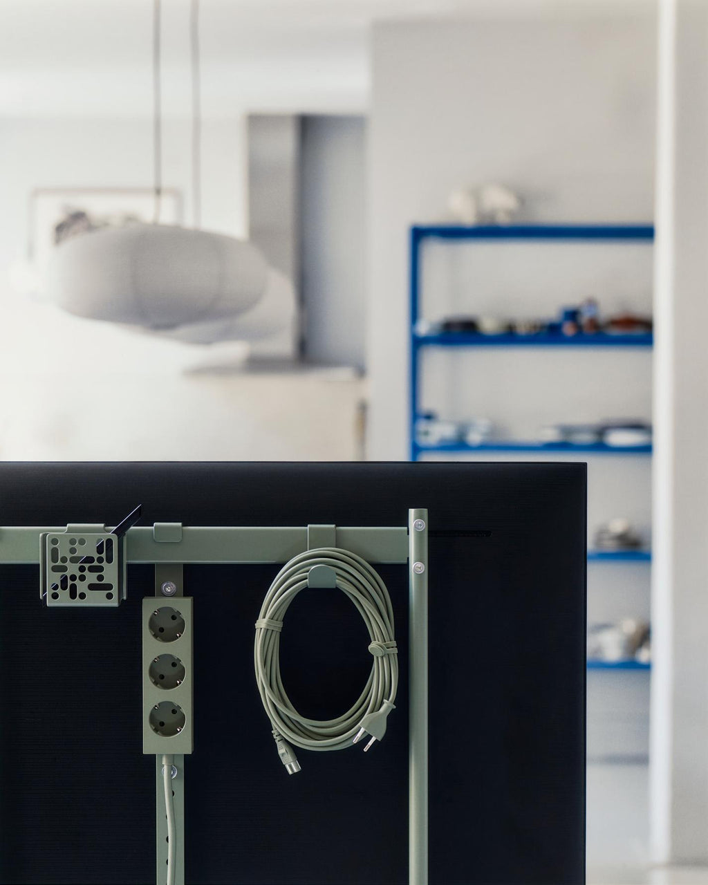 Mossy Green Remote Box Mount clipped to a TV stand frame beside a coiled cable and power strip in a bright studio