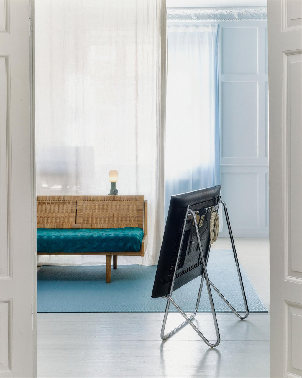 Sandstorm Remote Box Mount holding cables on a floor-stand TV's rear panel in a bright blue-toned living room