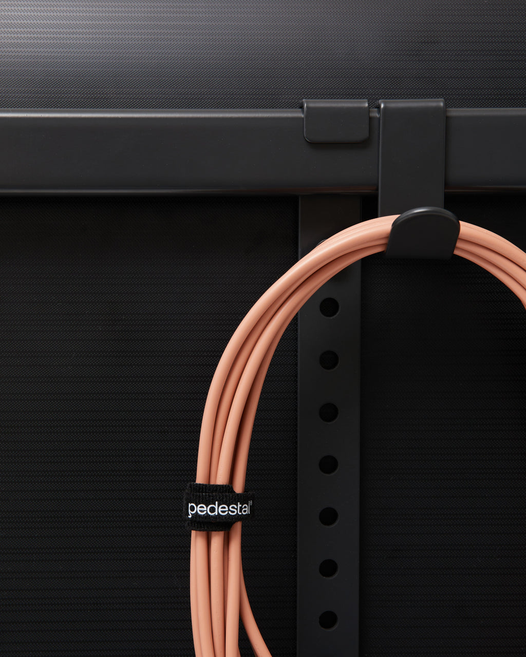 Black Velcro Cable Tie bundling a coiled salmon cable hung on a hook beneath a dark desk frame, close-up detail