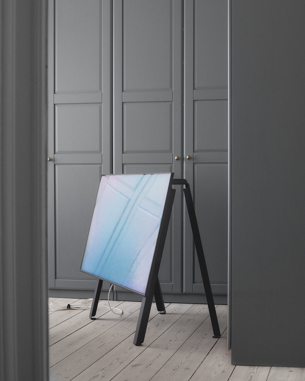 Black velcro cable ties bundling a TV power cord on a pale wood floor beside an easel-style screen stand