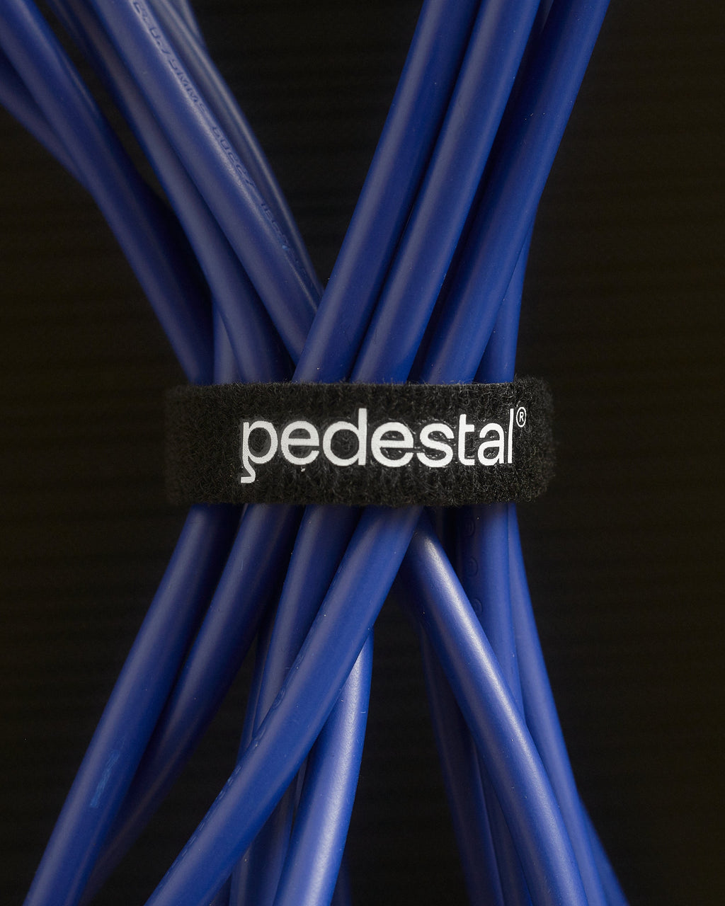 Black Velcro Cable Tie with white Pedestal logo wrapped around a bundle of blue cables, close-up studio detail shot