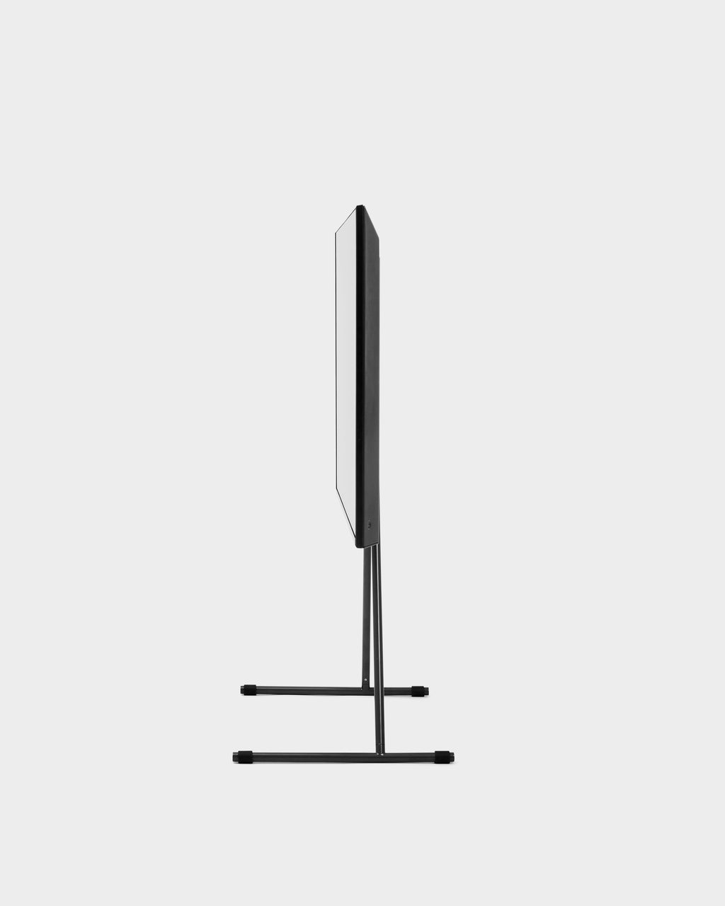 Side profile studio view of the Viva TV stand in Charcoal, mounted TV shown edge-on above its slim T-shaped legs