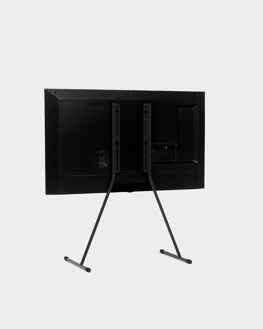Rear three-quarter studio view of the Viva TV stand in Charcoal with mounted TV, showing angled legs and VESA bracket