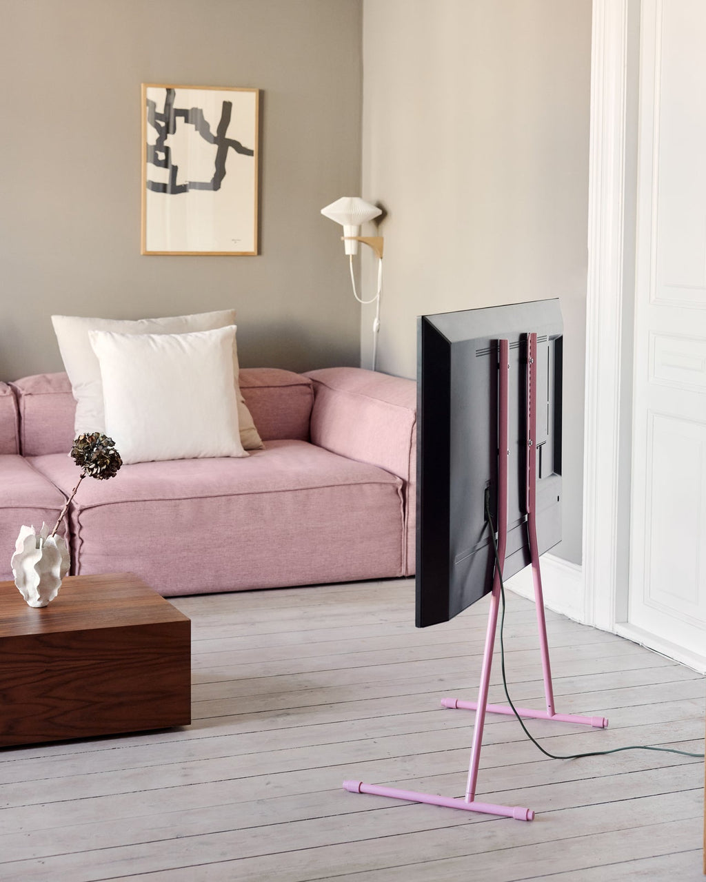 Rear view of Viva TV stand in Charcoal with pink legs holding a TV in a living room with pink sofa and wood table