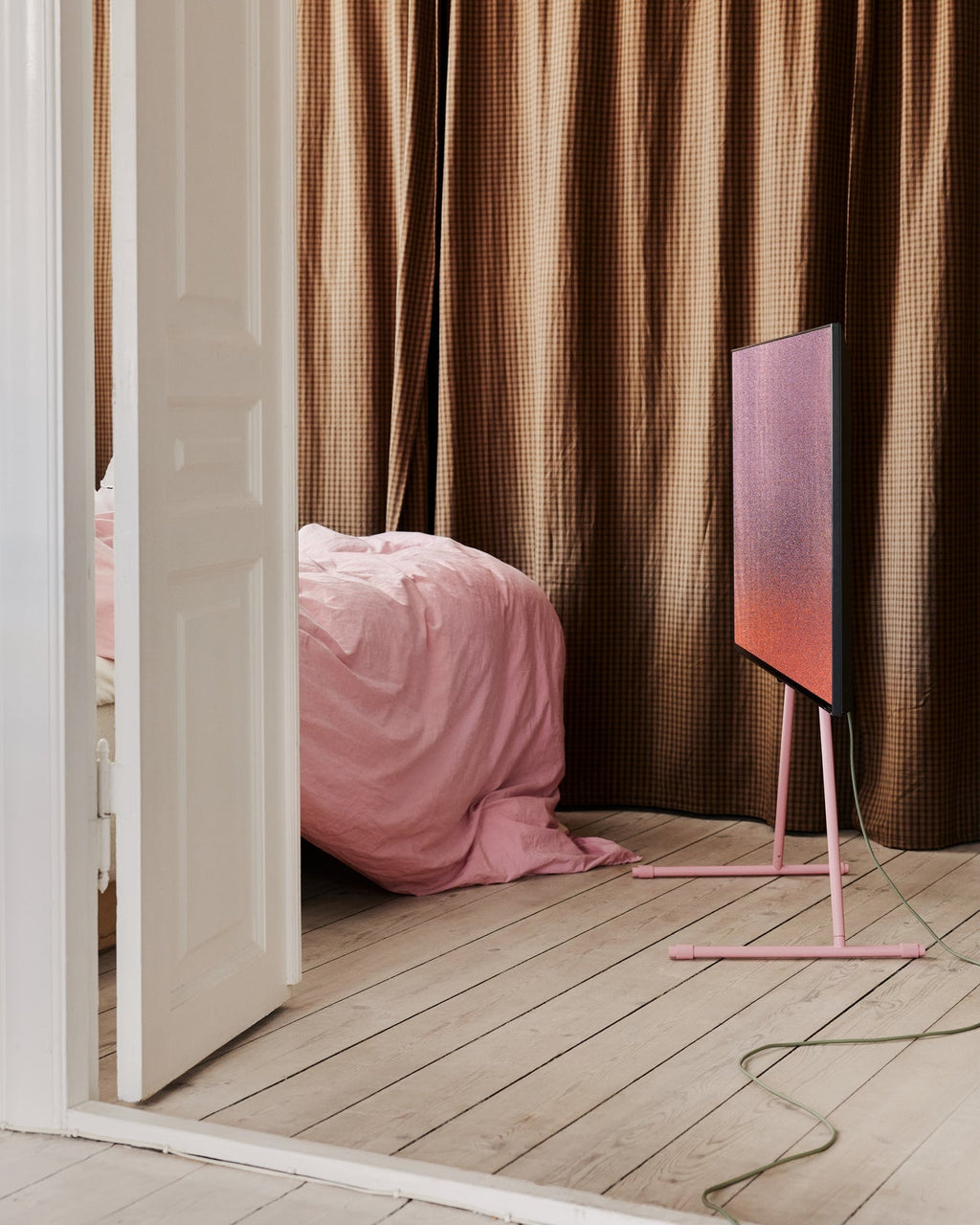 Viva TV stand in Bubble Gum pink holding a vertical screen in a bedroom with checked curtains and pink bedding