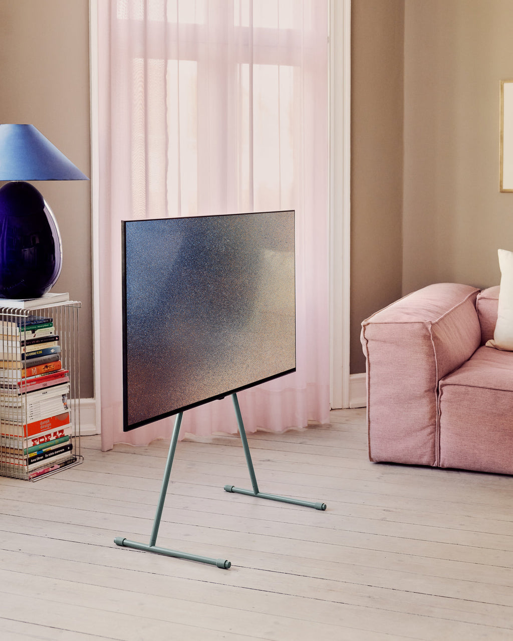 Viva TV stand in Mossy Green holding a large TV in a bright living room with pink sofa, sheer curtains and book rack