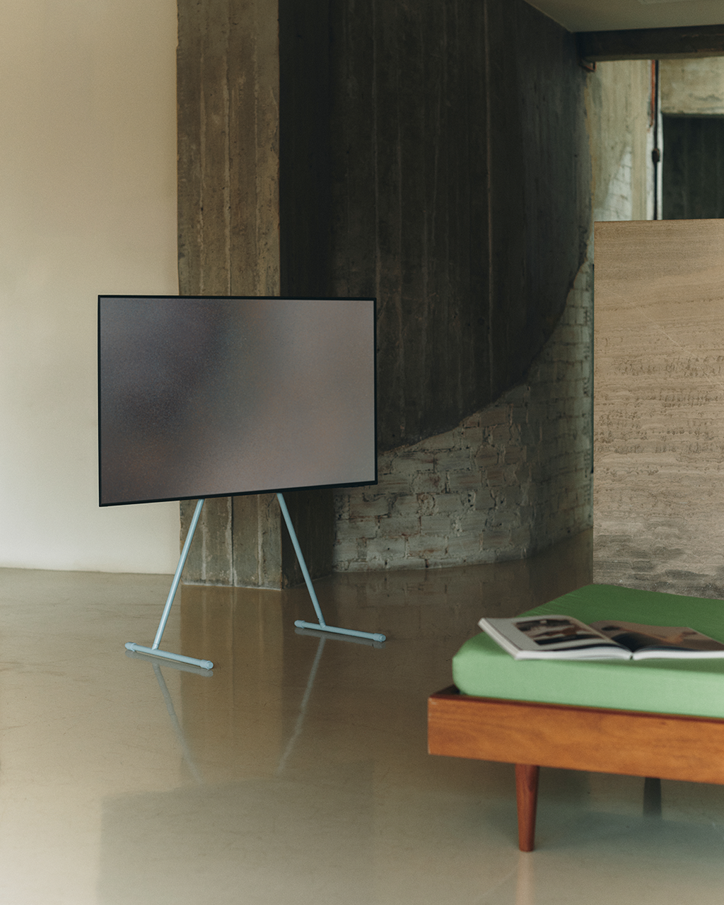Viva TV stand in Powder Blue holding a flat-screen TV in a concrete loft beside a green daybed with an open book