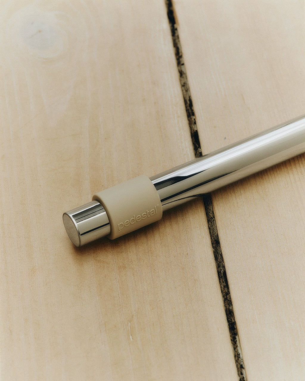 Close-up of the Viva in Chrome TV stand's polished pole end and beige branded collar resting on pale wood planks